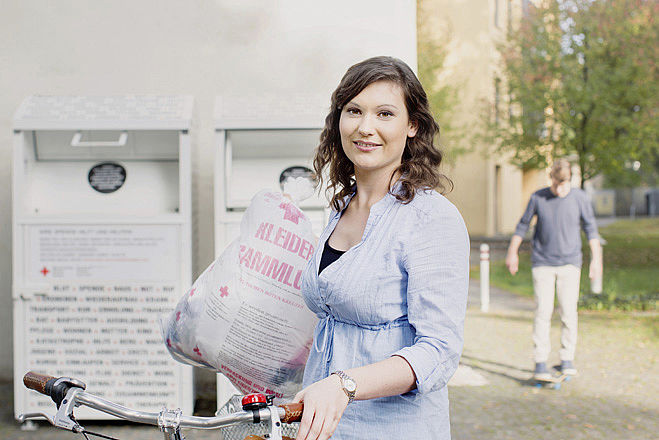 Kleidersammlung des DRK und Altkleidercontainer: junge Frau mit Altkleidersack vor einem Container des DRK- 2014